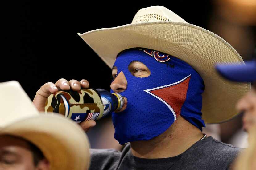 A Texas Rangers fan wearing a cowboy hat and a wrestling mask drinks beer during a baseball...