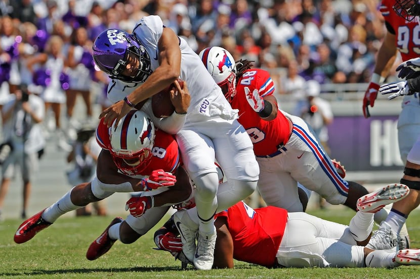 TCU Horned Frogs quarterback Kenny Hill (7) gets hit by SMU defenders while running the ball...