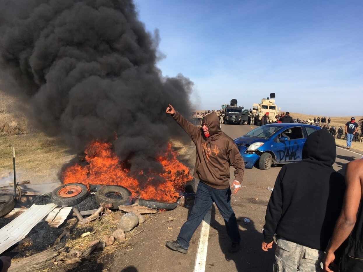 Demonstrators stand next to burning tires as armed soldiers and law enforcement officers...