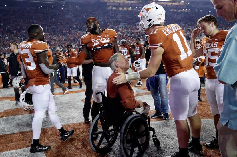 Texas Gov. Greg Abbott, center in wheelchair, visits with Texas quarterback Sam Ehlinger...