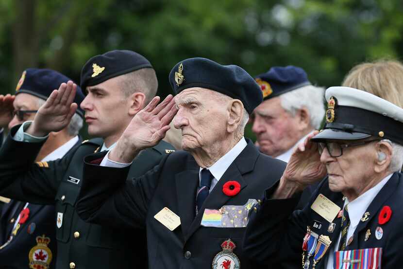 Canadian World War II veteran Dick Brown (second from right) and Rod Deon (right) salute as...