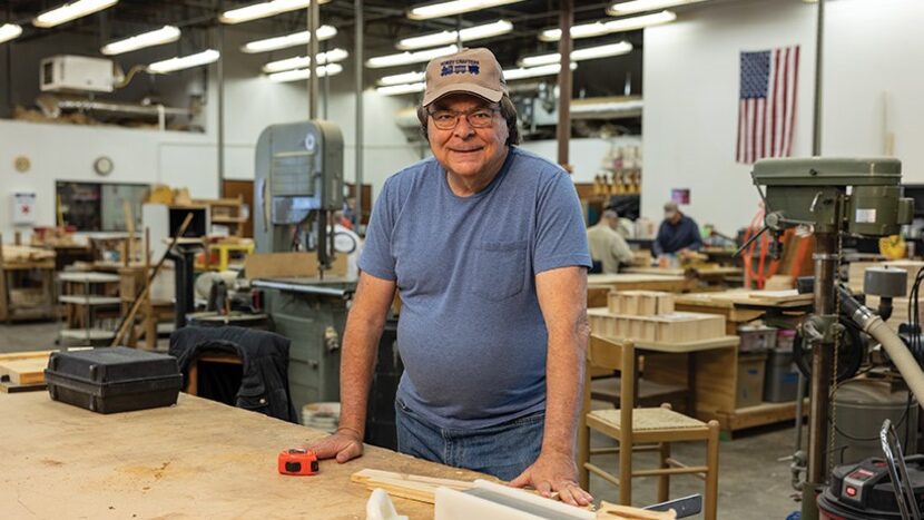 Man smiles while standing at woodworking table