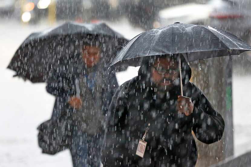 Pedestrians walk through a downpour as they arrive at the Earle Cabell federal courthouse,...