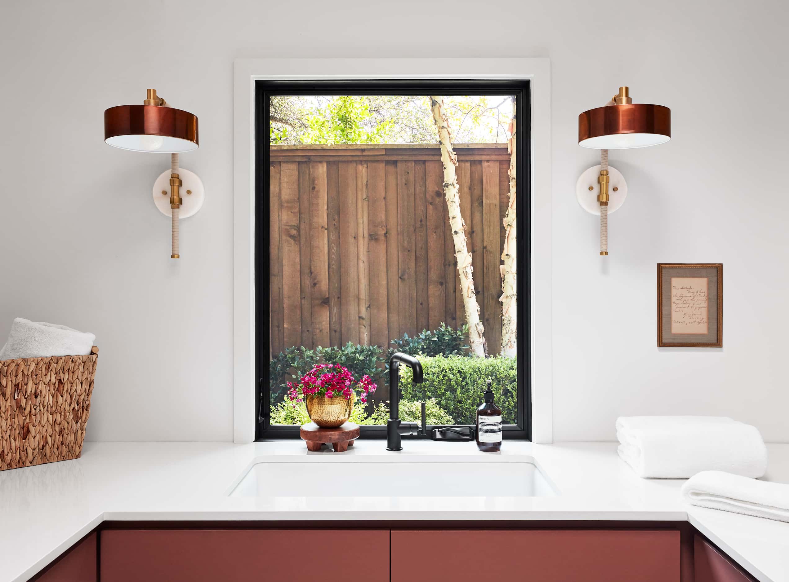 Laundry room sink in front of window with red cabinets beneath, red sconces frame window