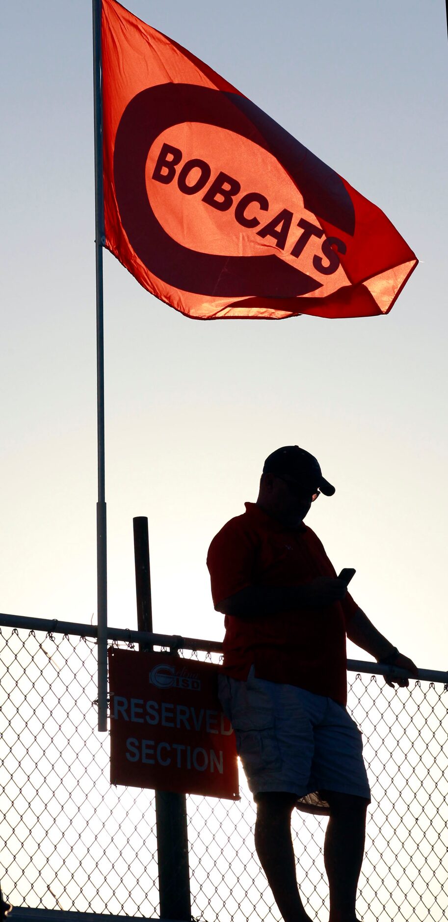 (TXHSFB) A Celina High fan checks his mobile phone under a team flag before the start of a...