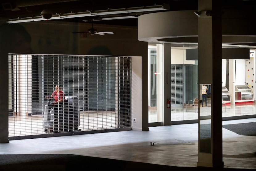 Passing by empty stores, housekeeper Juana Lemoine polishes the floor of an empty Collin...