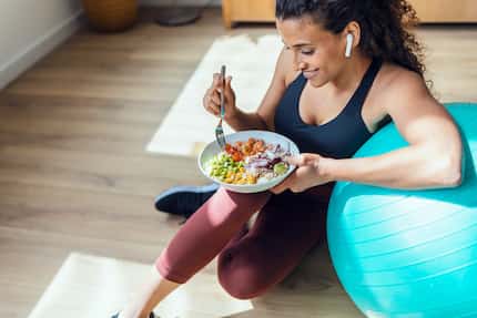 Shot of sporty young woman eating healthy while listening to music sitting on the floor at...