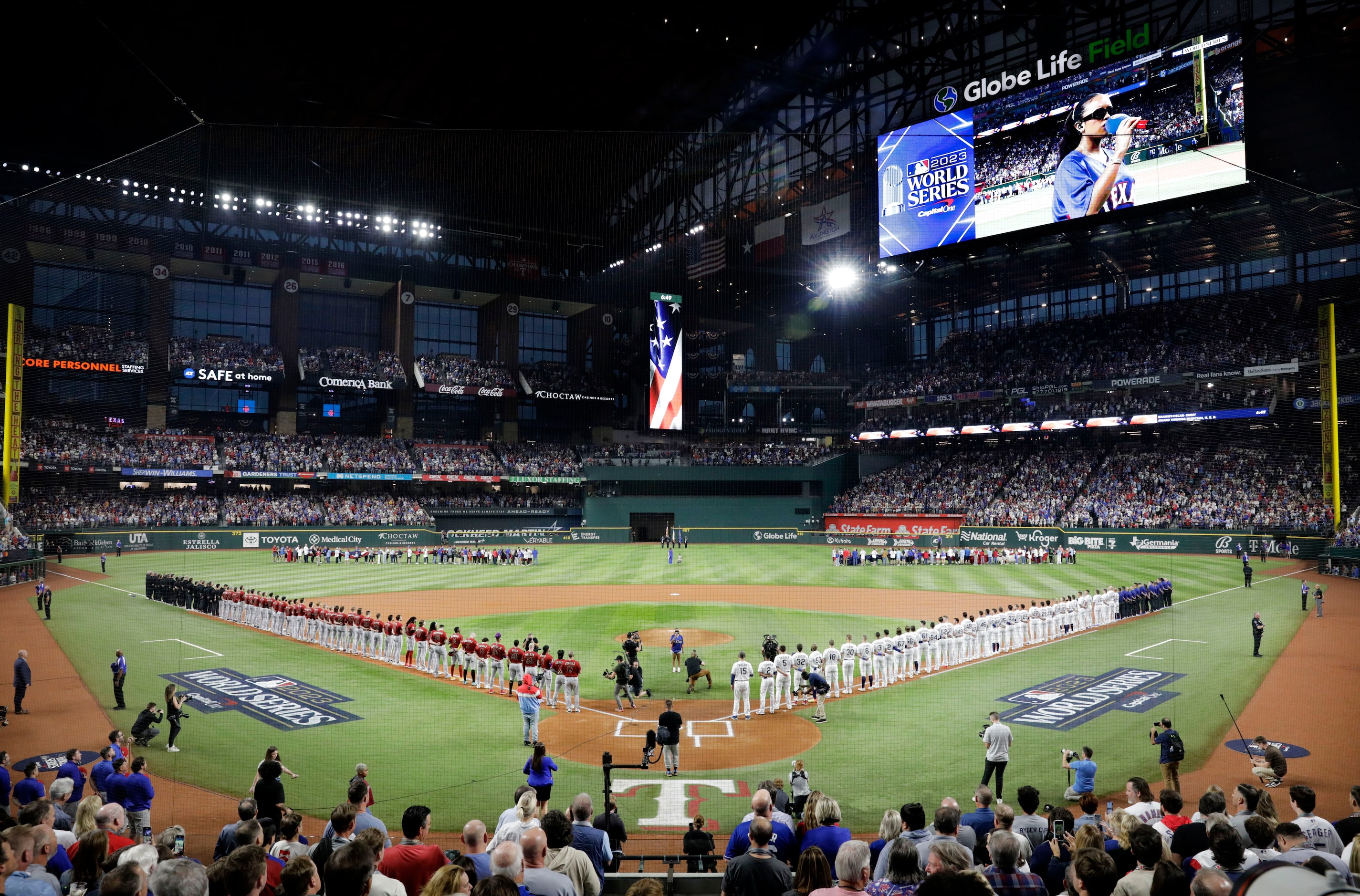 The Texas Rangers and Arizona Diamondbacks players and coaches line the base paths as H.E.R...