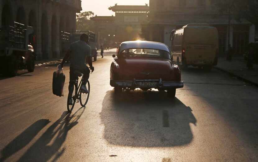 
A man on a bike balances bread in one hand as he rides behind a cab in Havana. 
