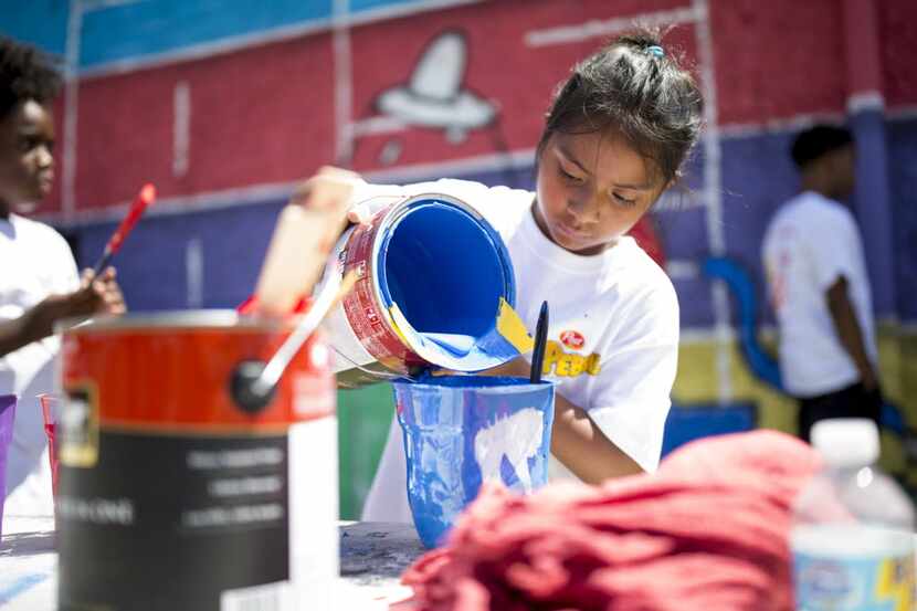 Brielle Yanez, 8, pours paint into buckets for painting the mural designed by her brother,...