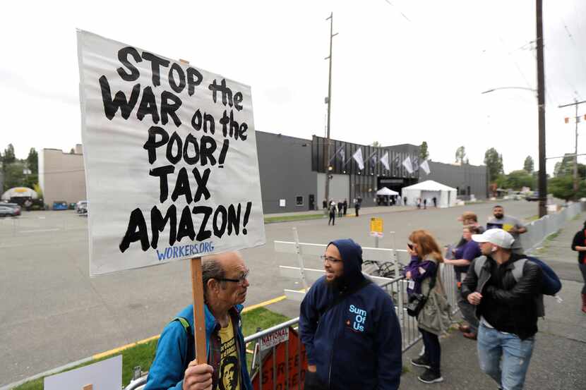 A protester holds a sign that reads "Stop the war on the poor! Tax Amazon!" as he stands...