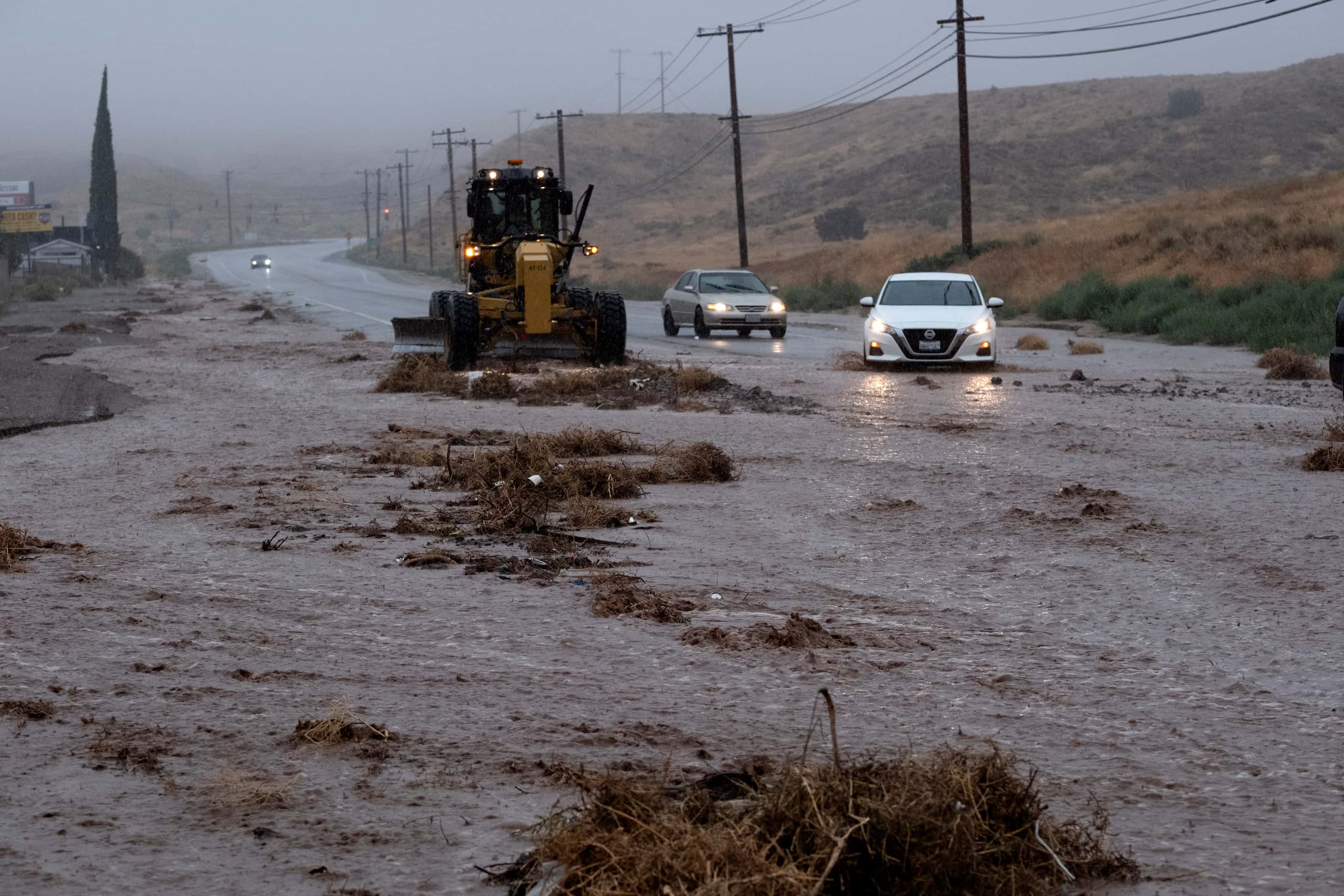 Cars maneuver around a plow clearing debris along a flooded Sierra Highway in Palmdale,...