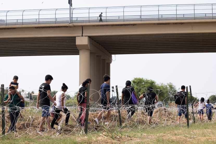 Migrants walk by razor wire fencing after crossing the Rio Grande from Mexico into the U.S....