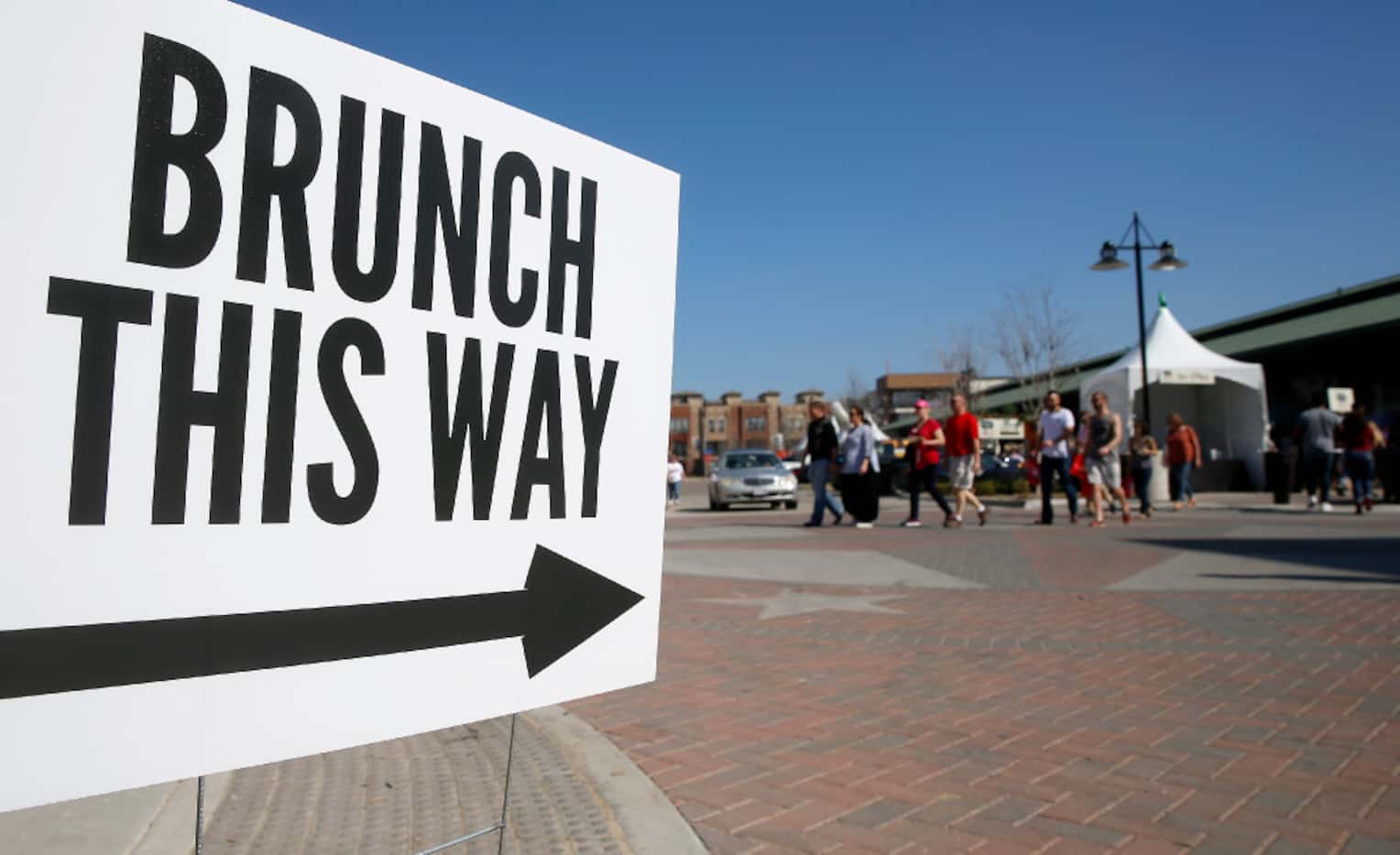 People walk by a sign during Morning After Brunch Festival at Dallas Farmers Market in...