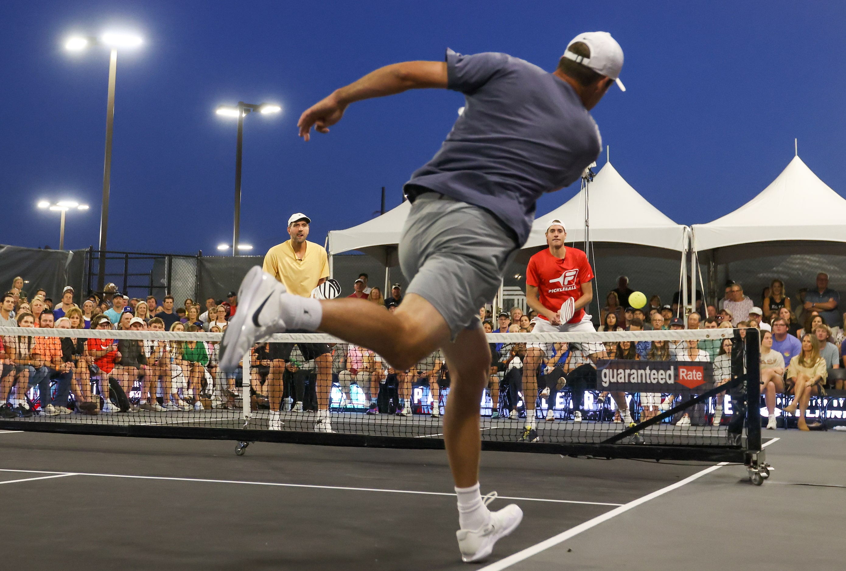 Scottie Scheffler (center) leaps to hit the ball toward Dirk Nowitzki and John Isner in a...