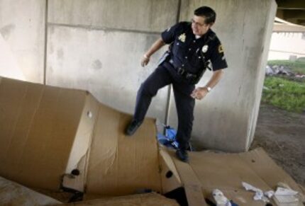  Dallas Police Officer Robert Garcia stomps down a homeless shanty under I-45 and Louise...