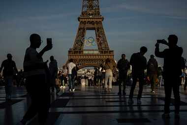 People photograph and film the Olympic rings that are displayed on the Eiffel Tower Friday,...