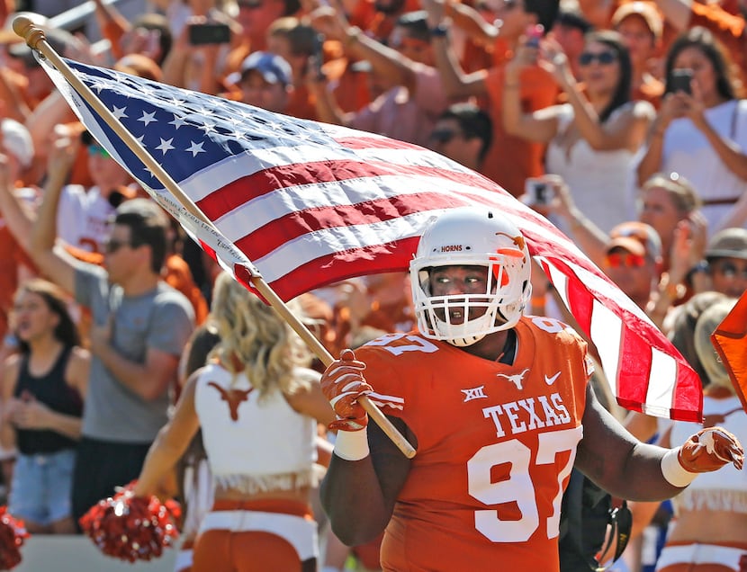 Texas Longhorns defensive lineman Chris Nelson (97) carries the American flag onto the field...