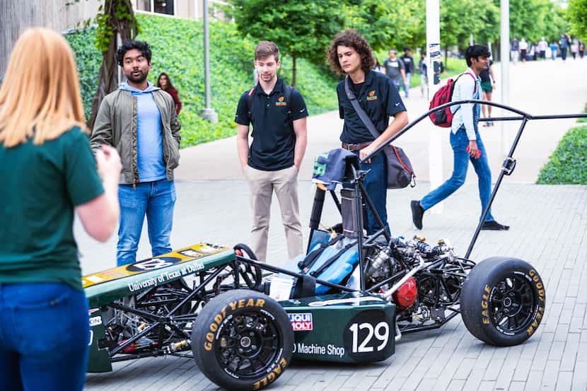 A Formula Racing car sits in foreground with students looking on.
