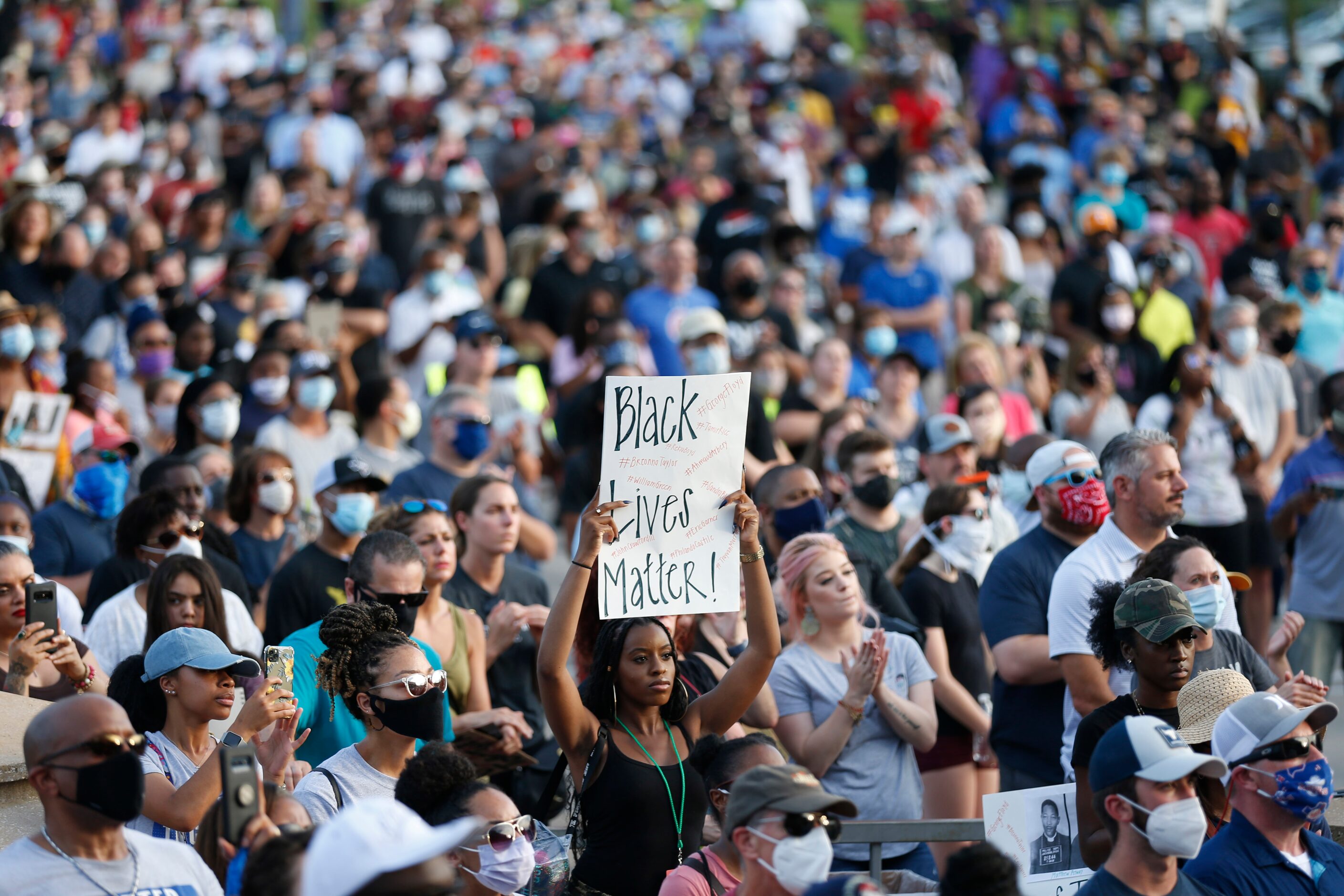 A woman holds up a sign as people stand together during a prayer vigil as various pastors...