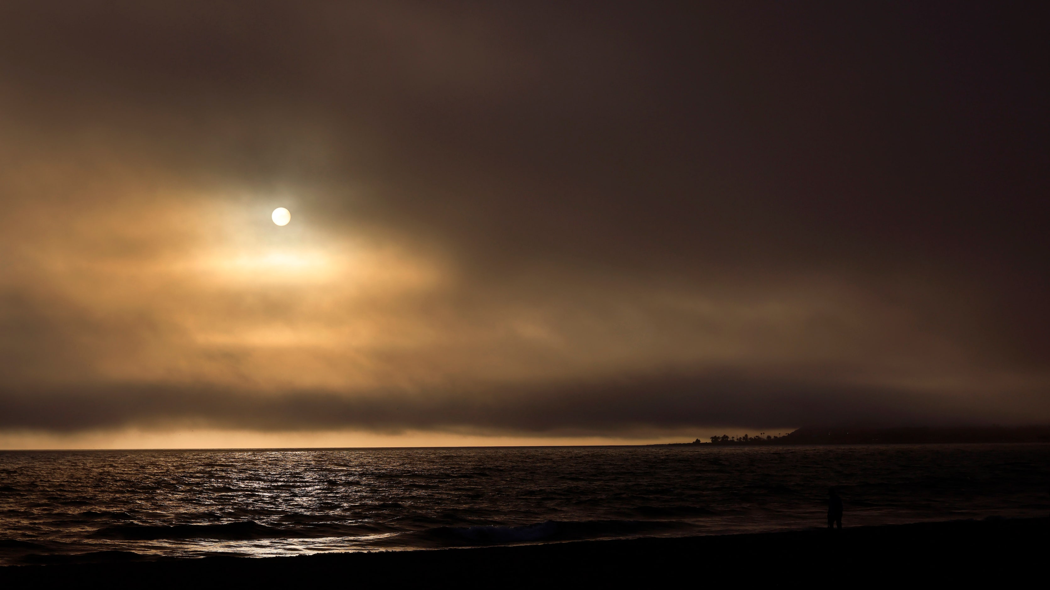 The sun setting over the Pacific Ocean appears through a thick marine layer of air in...