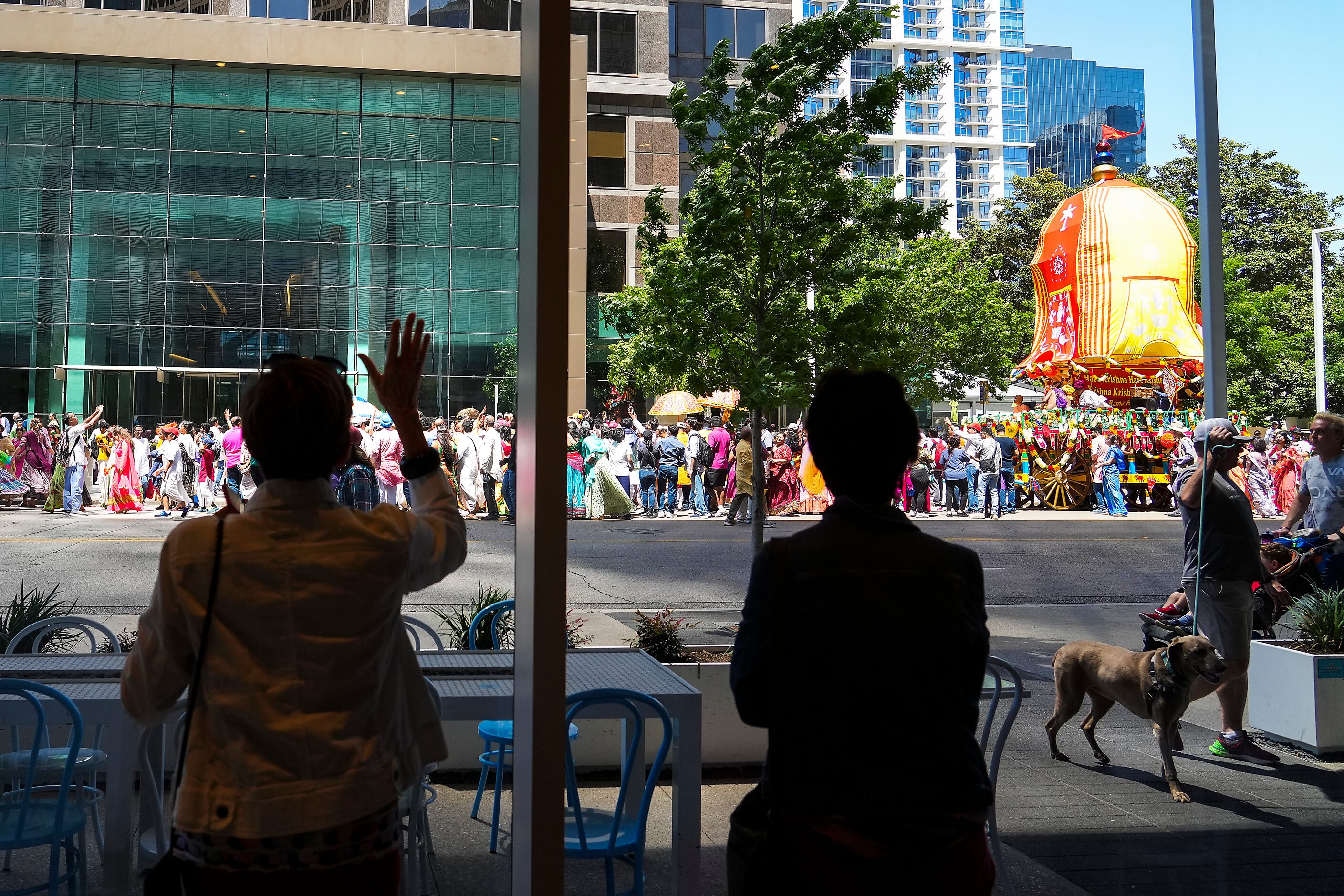 People inside a sandwich shop on Ross Avenue wave as the Ratha Yatra parade parade passes...