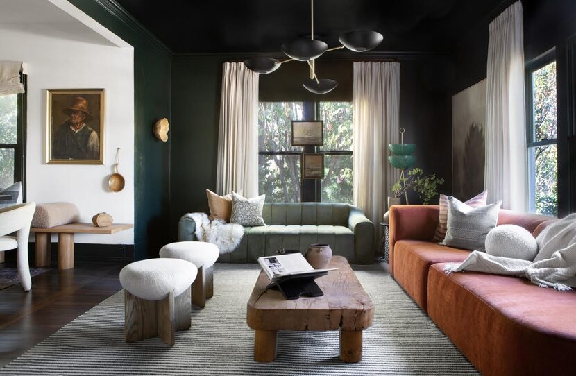 Black-walled sitting room with pink sofa, white stools and cream curtains, low wooden table...