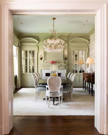 A dining room has green millwork throughout and cabinets on one end surrounding a fireplace.