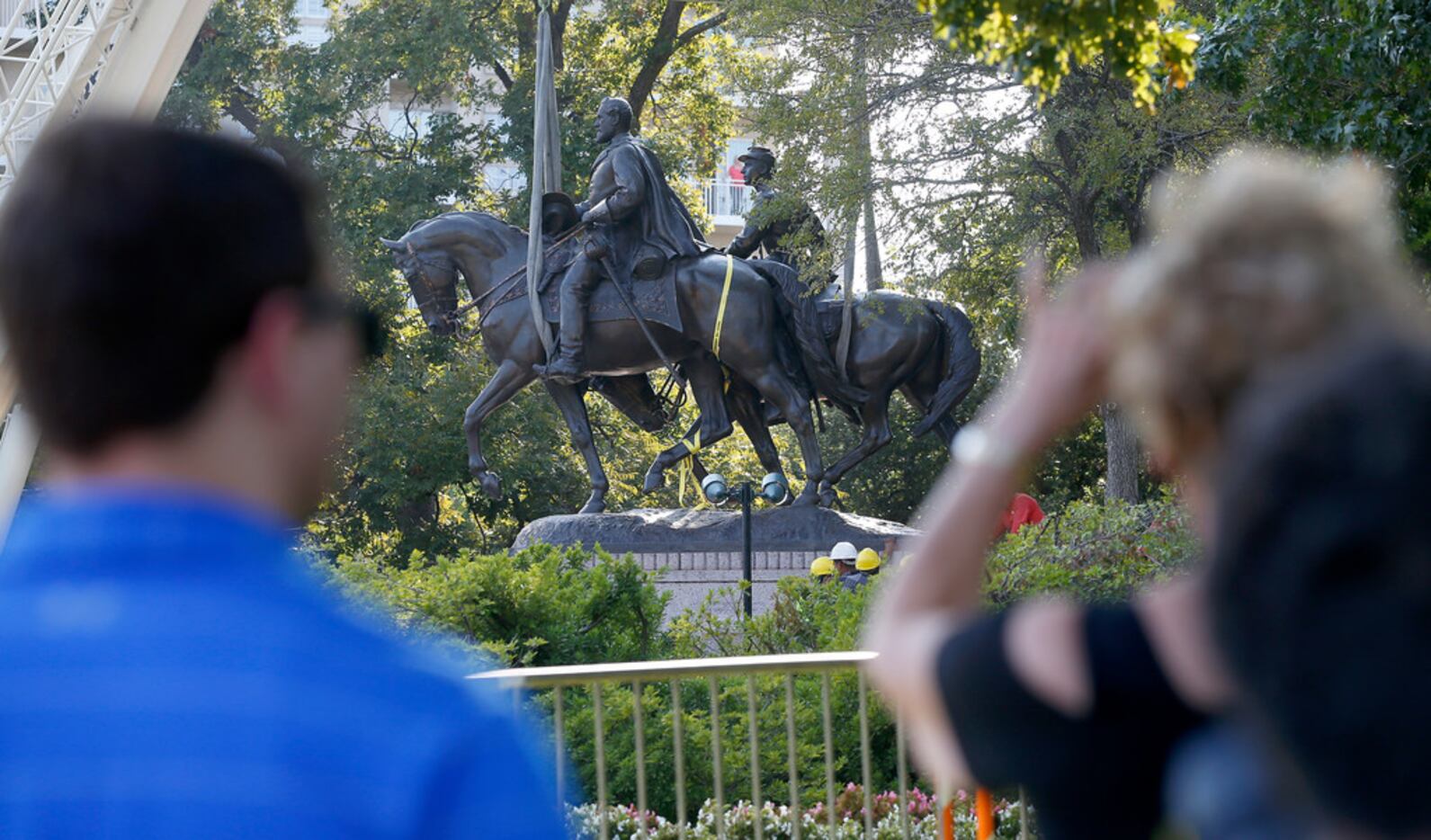 People watch crew members work to remove the Robert E. Lee statue at Robert E. Lee Park in...