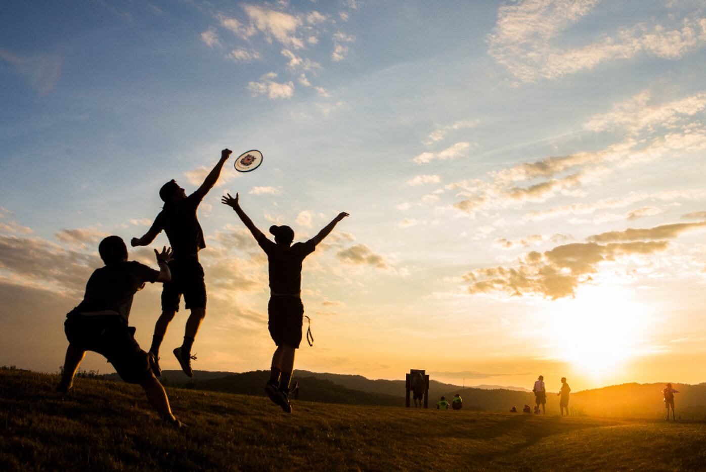 Venturers Isaac Peterson, Carden Hansen, and Mitchner Whalen play Frisbee as the sun sets.