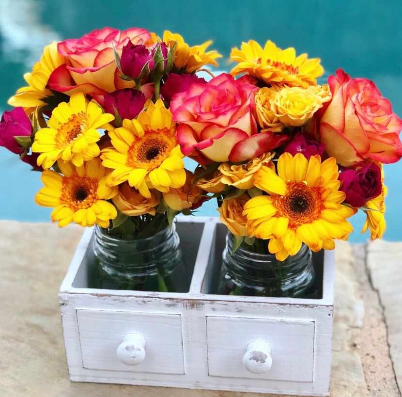 White drawer with two mason jars inside, containing a bouquet of sunflowers and roses