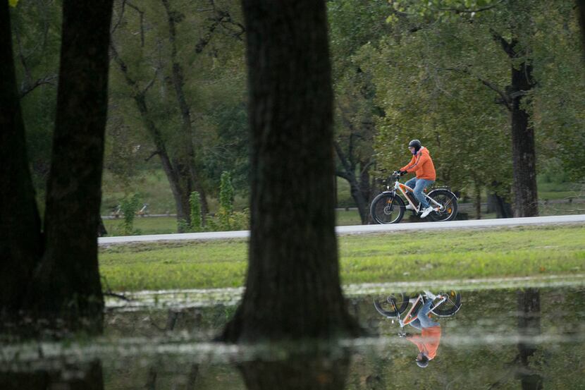 A cyclist is reflected in water left standing after recent heavy rains while riding along...
