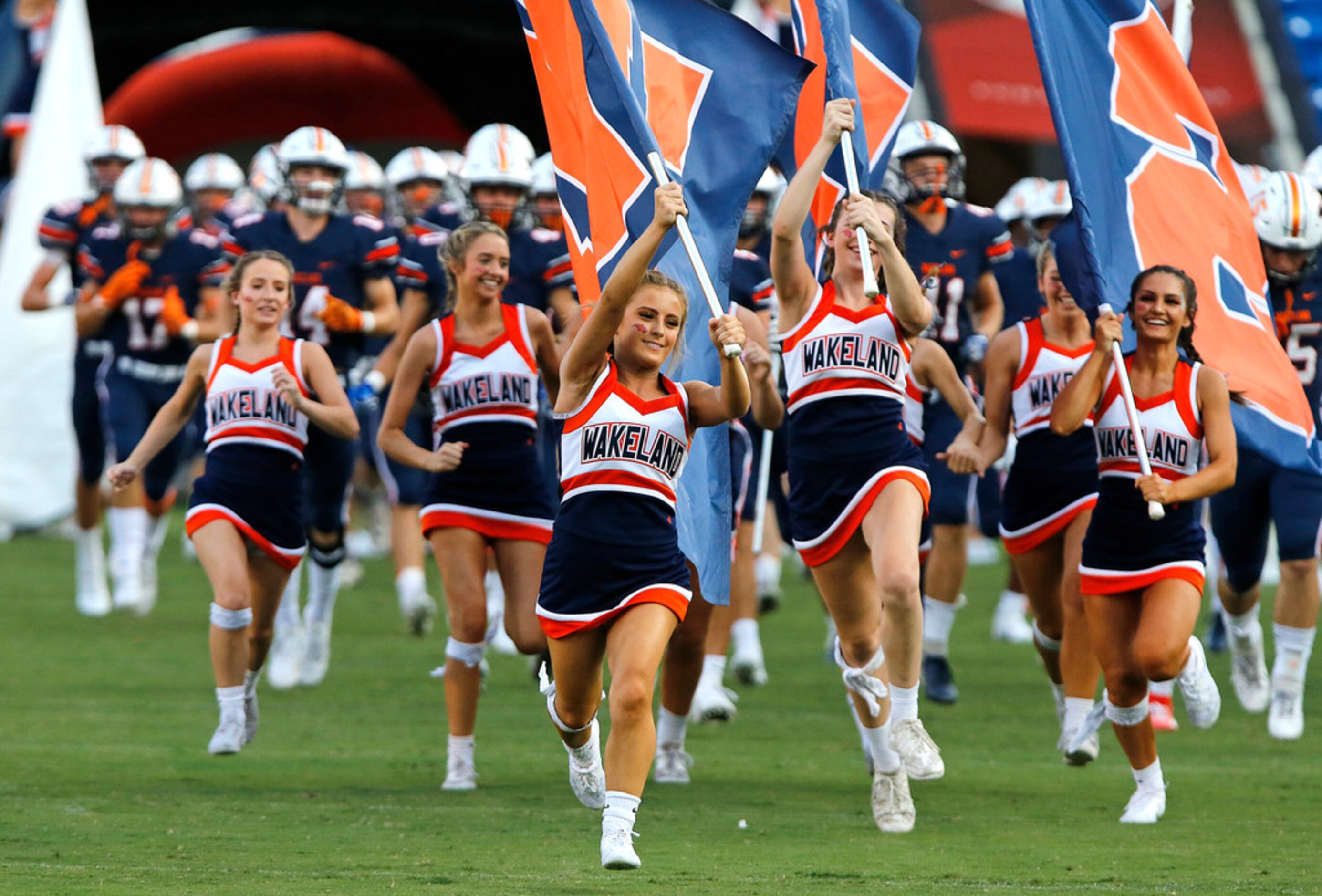 Wakeland High School cheerleader Lily Lawrence (center) runs a team flag in front of the...