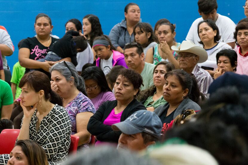 Community members listen to announcements during a community meeting regarding upcoming mass...