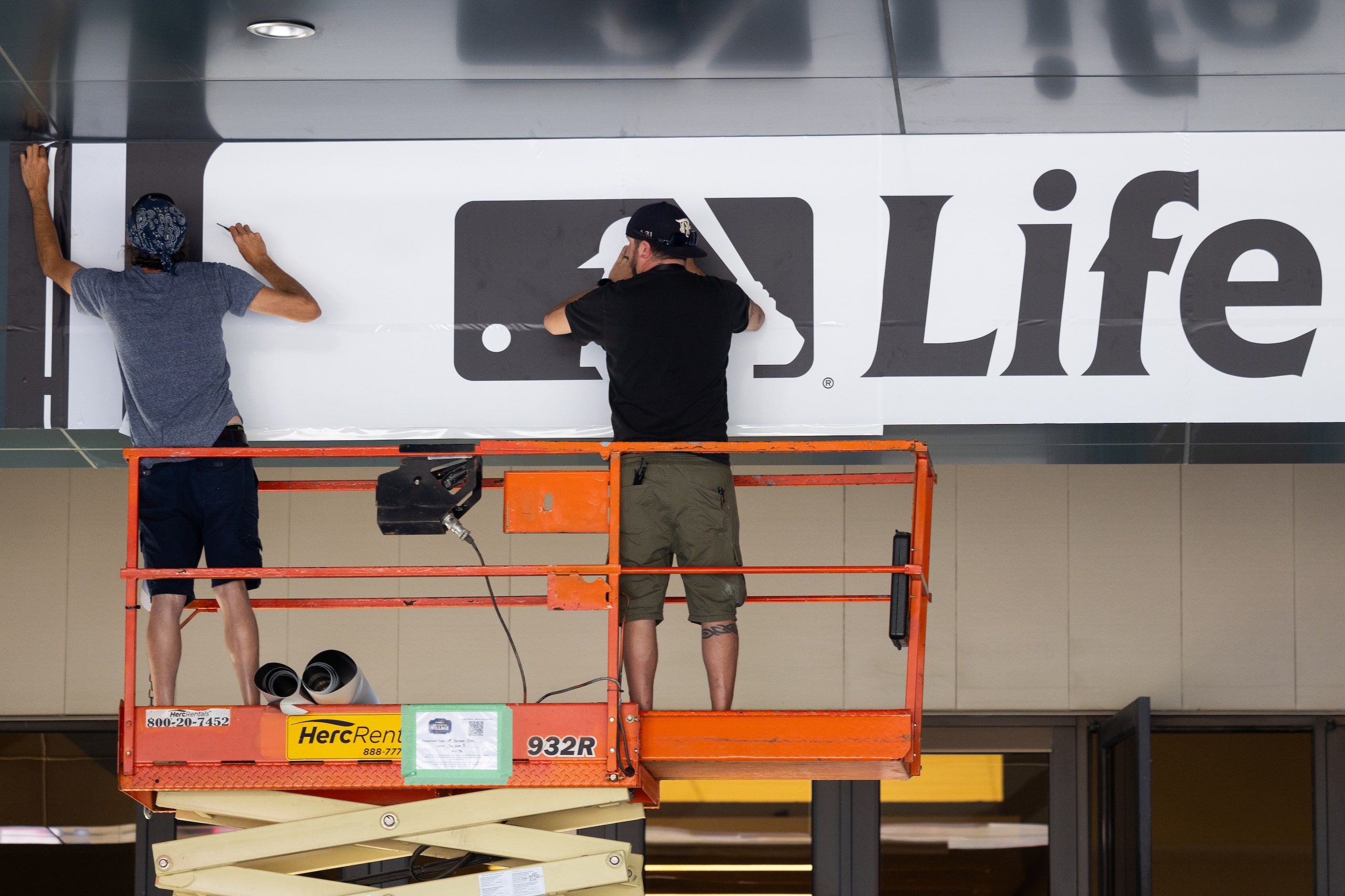 Workers place an MLB Life banner at the MLB's All-Star Village installation at the Esports...