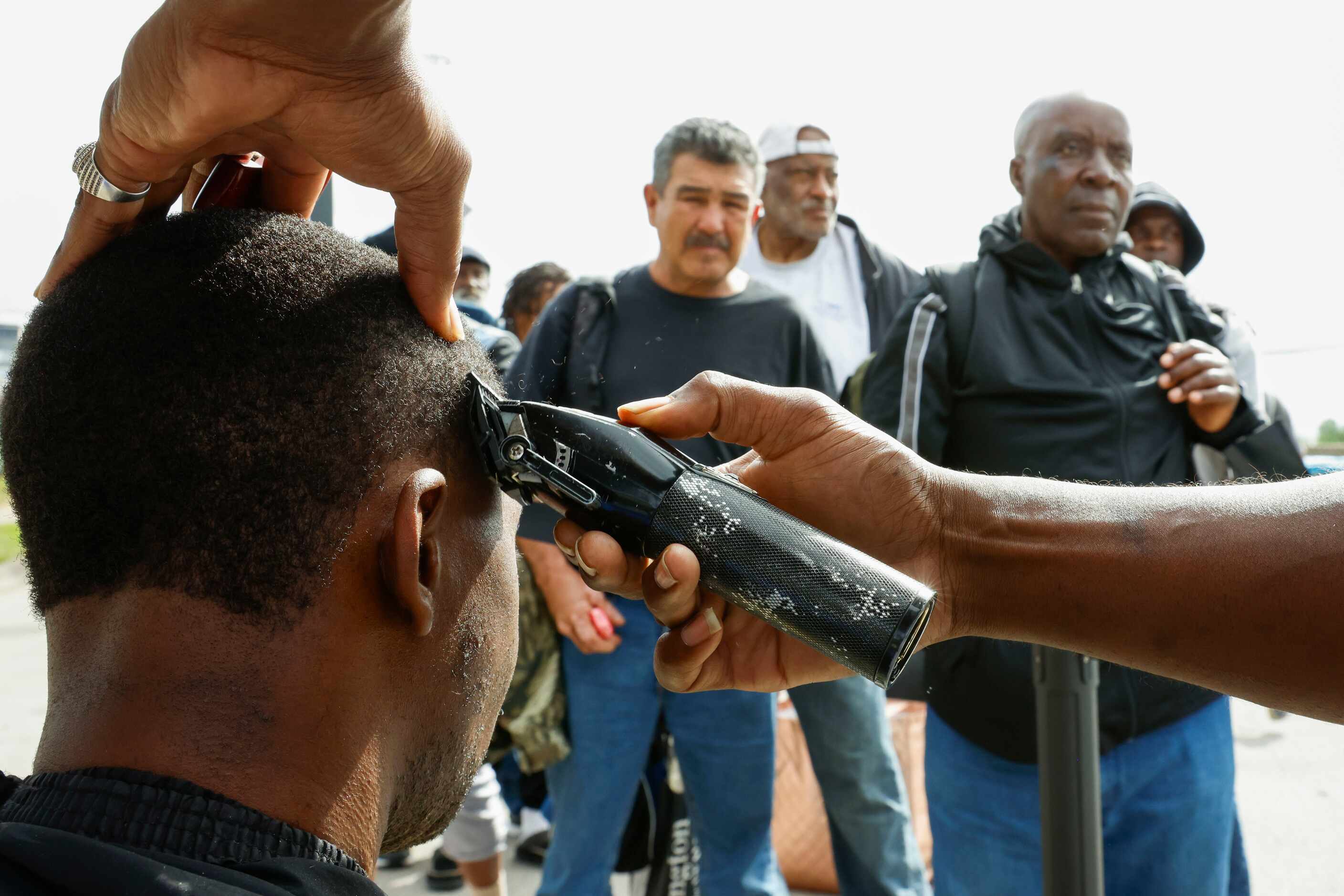 People wait as barber King Jaymes Bell (right) gives haircut to an individual during first...