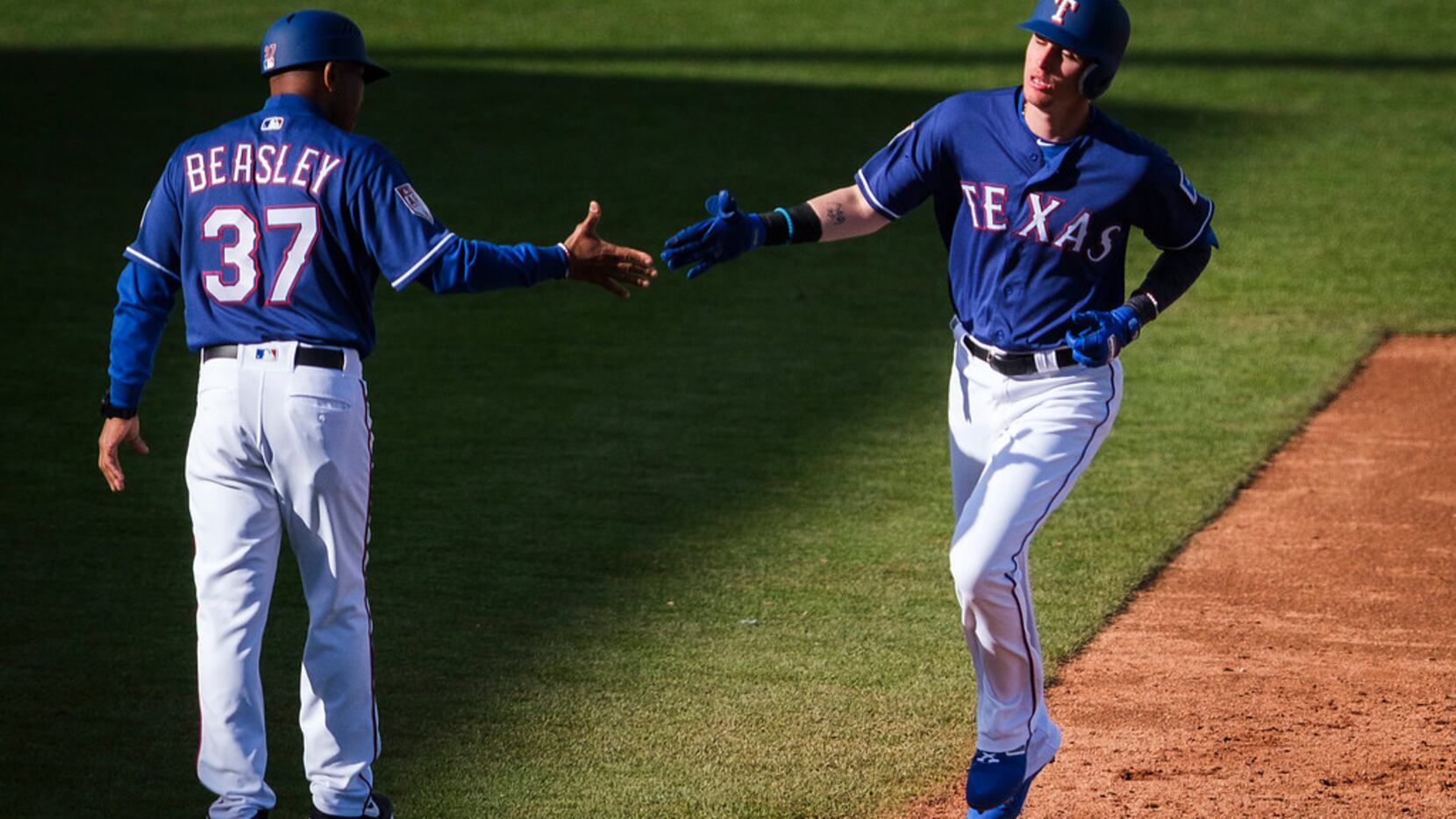 Texas Rangers outfielder Carlos Tocci gets a hand from third base coach Tony Beasley (37) as...