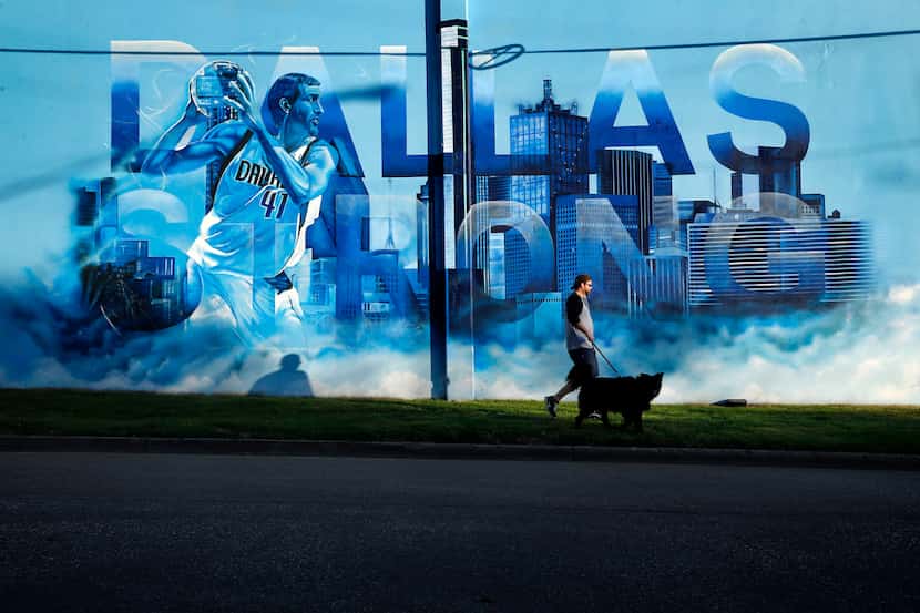 Scott Mitchell of Dallas walks his border collie Arthur past an image of Dallas Mavericks...