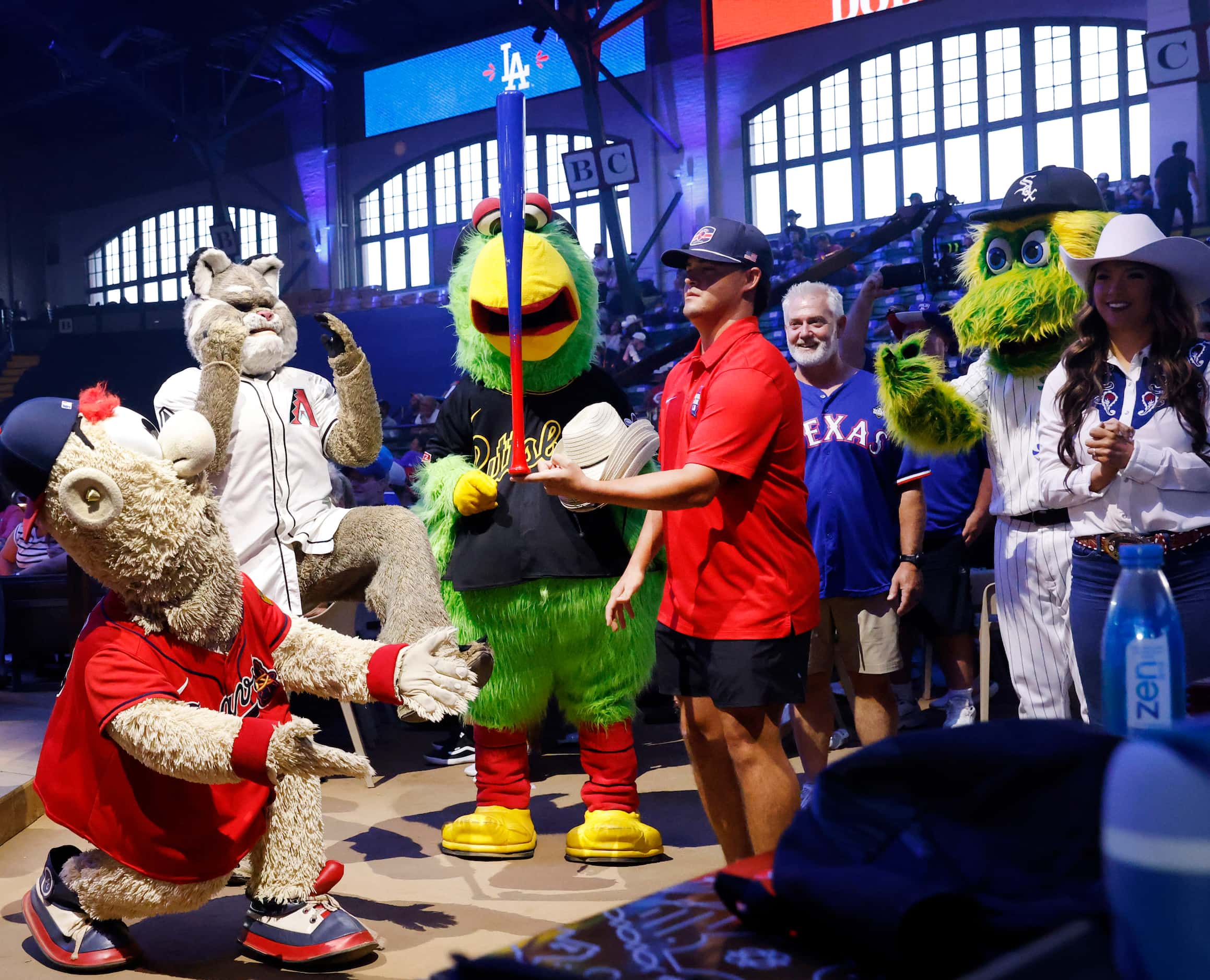 Major League mascots circle a fan who competed in a bat balancing competition during Day 1...