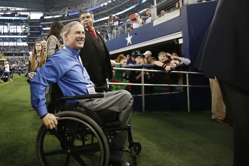Governor elect Greg Abbott waves to the crowd as he exits the field before a game between...