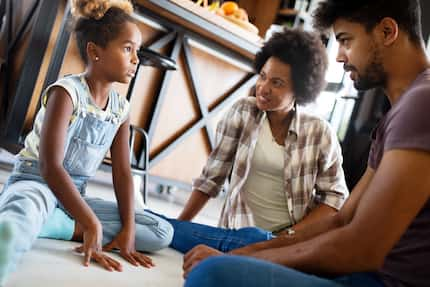 Parents having conversation with their child while sitting on the floor at home.