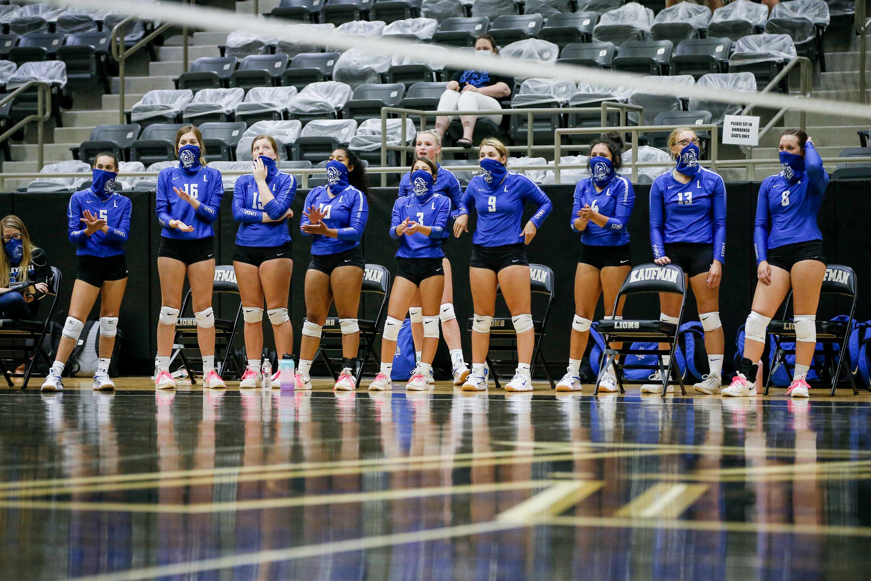 The Lindale varsity volleyball reserve players wear masks as they watch their teammates...