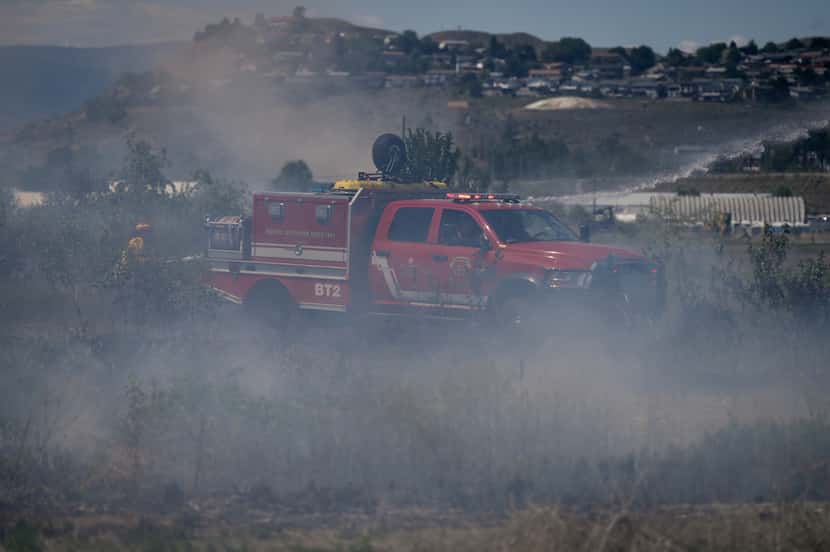 Firefighters battle a grass fire burning behind a residential property in Kamloops, British...