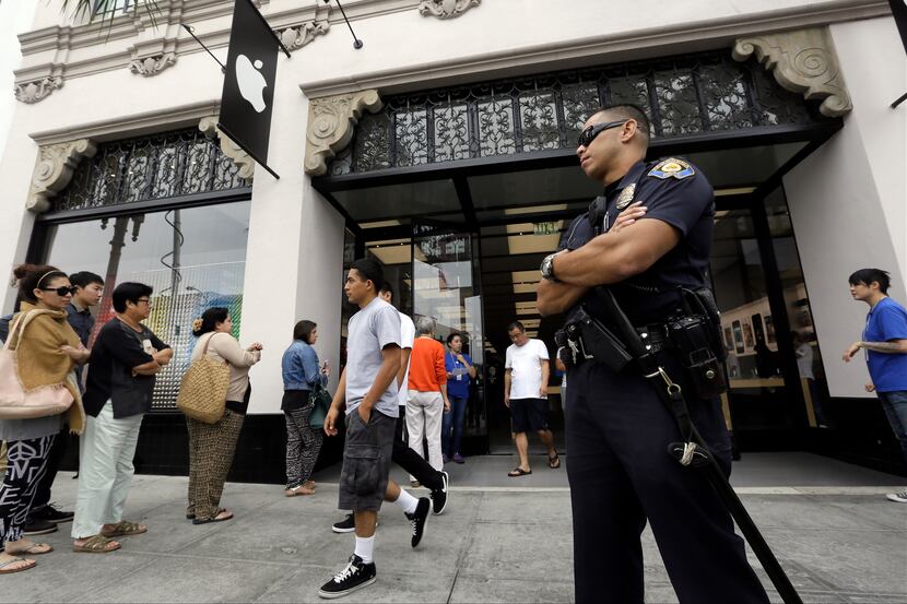 A police officer guards the entrance of the Apple store as customers wait in line for the...