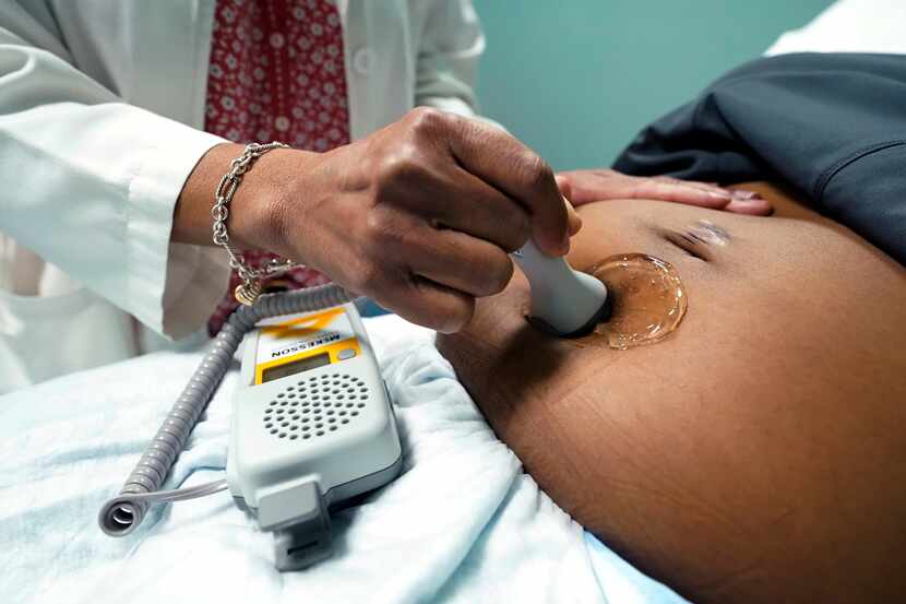 A doctor uses a hand-held Doppler probe on a pregnant woman to measure the heartbeat of the...