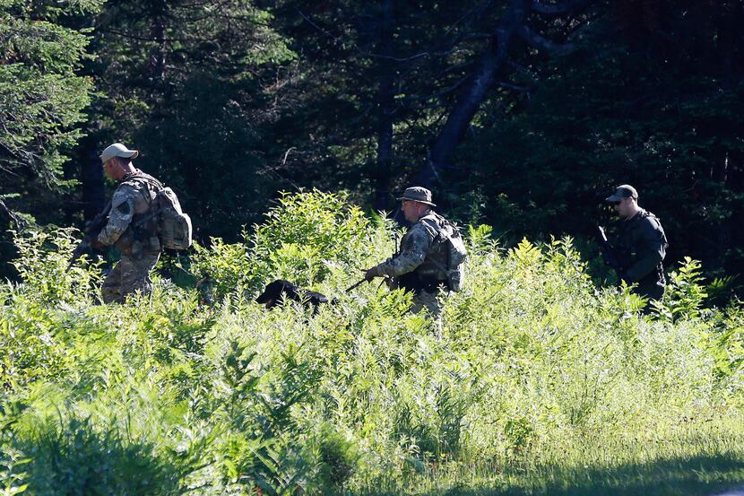 Law enforcement officers walk into the woods as the search continues for two escaped...