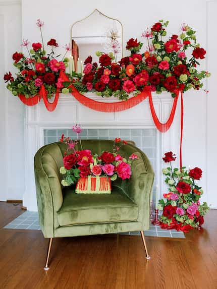 Red and pink flowers arranged on a mantel and on the floor, with more flowers in a green...