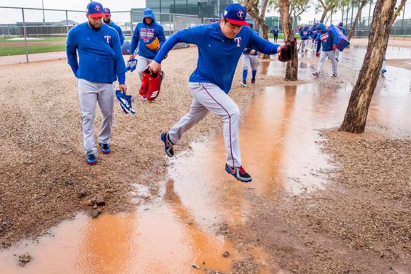 Texas Rangers outfielder Shin-Soo Choo leaps over standing water between practice fields as...