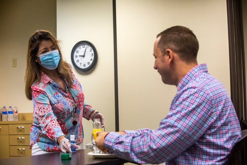 Administrative assistant Robbie Marquez (left) hands a hand sanitizer bottle to new hire and...