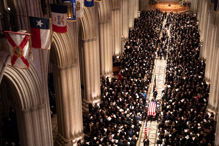 A military honor guard carries the flag-draped casket as it depart the Washington National...